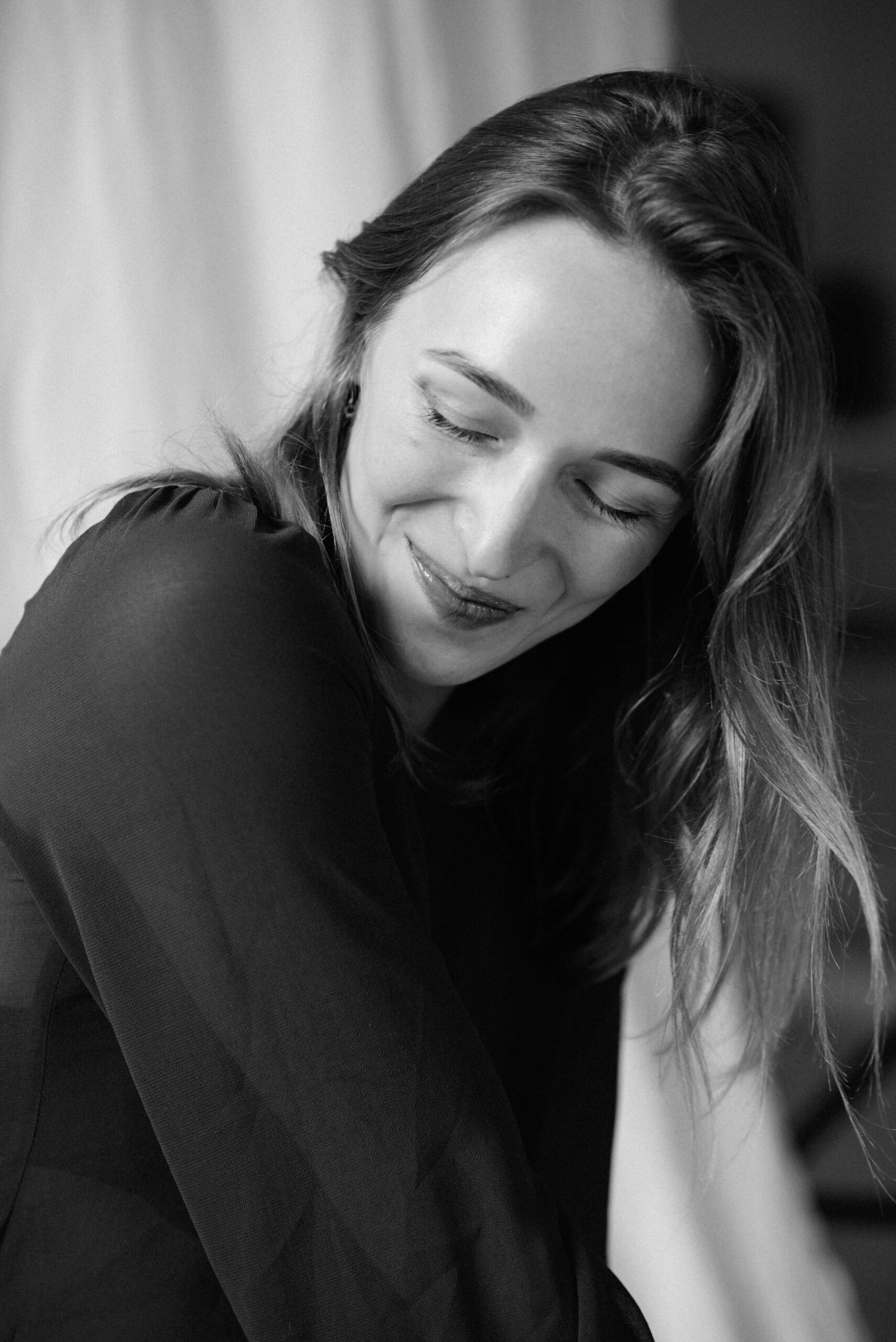 Black-and-white portrait of a smiling model in soft natural light.