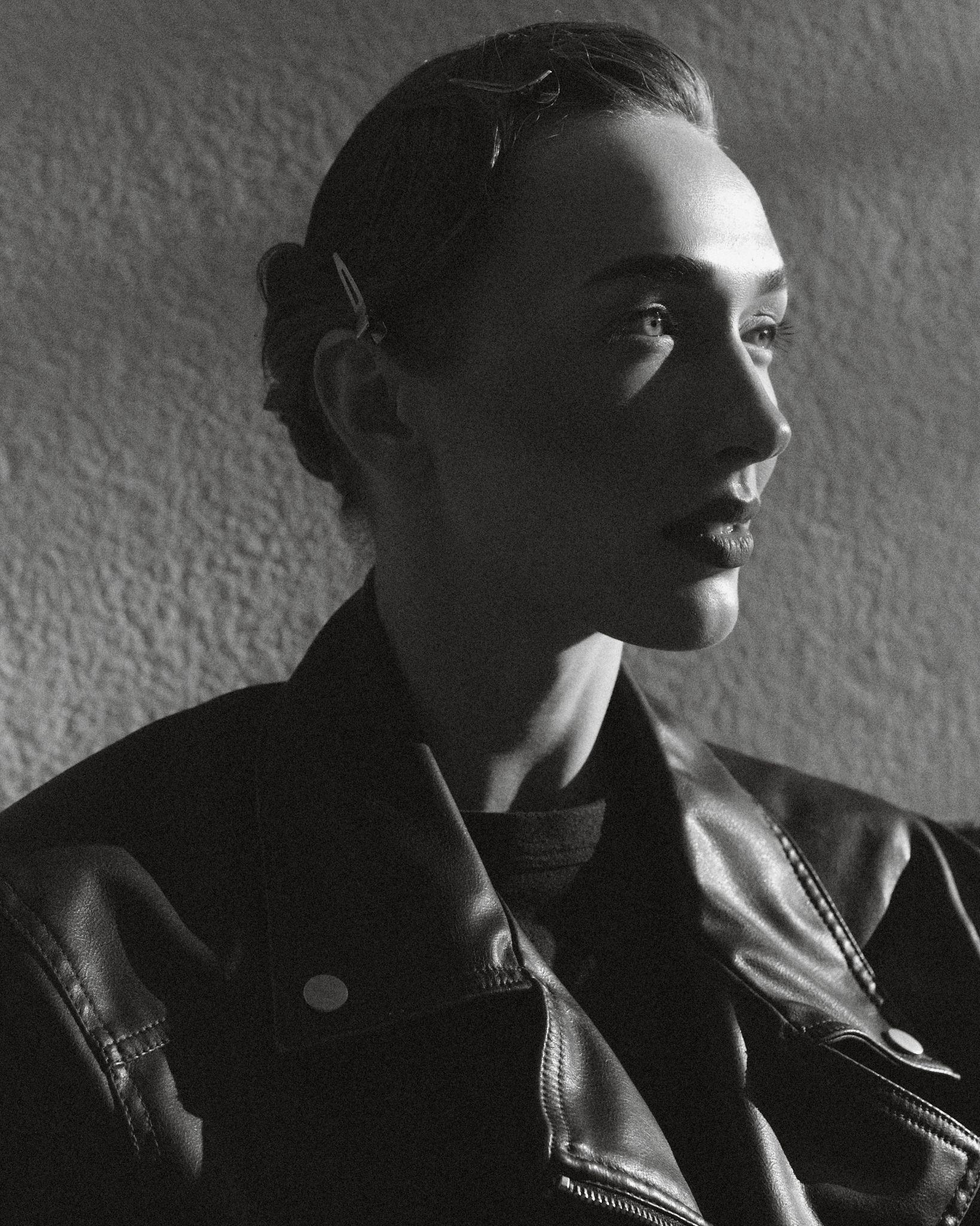 Black-and-white side-profile portrait in a leather jacket with dramatic natural light.