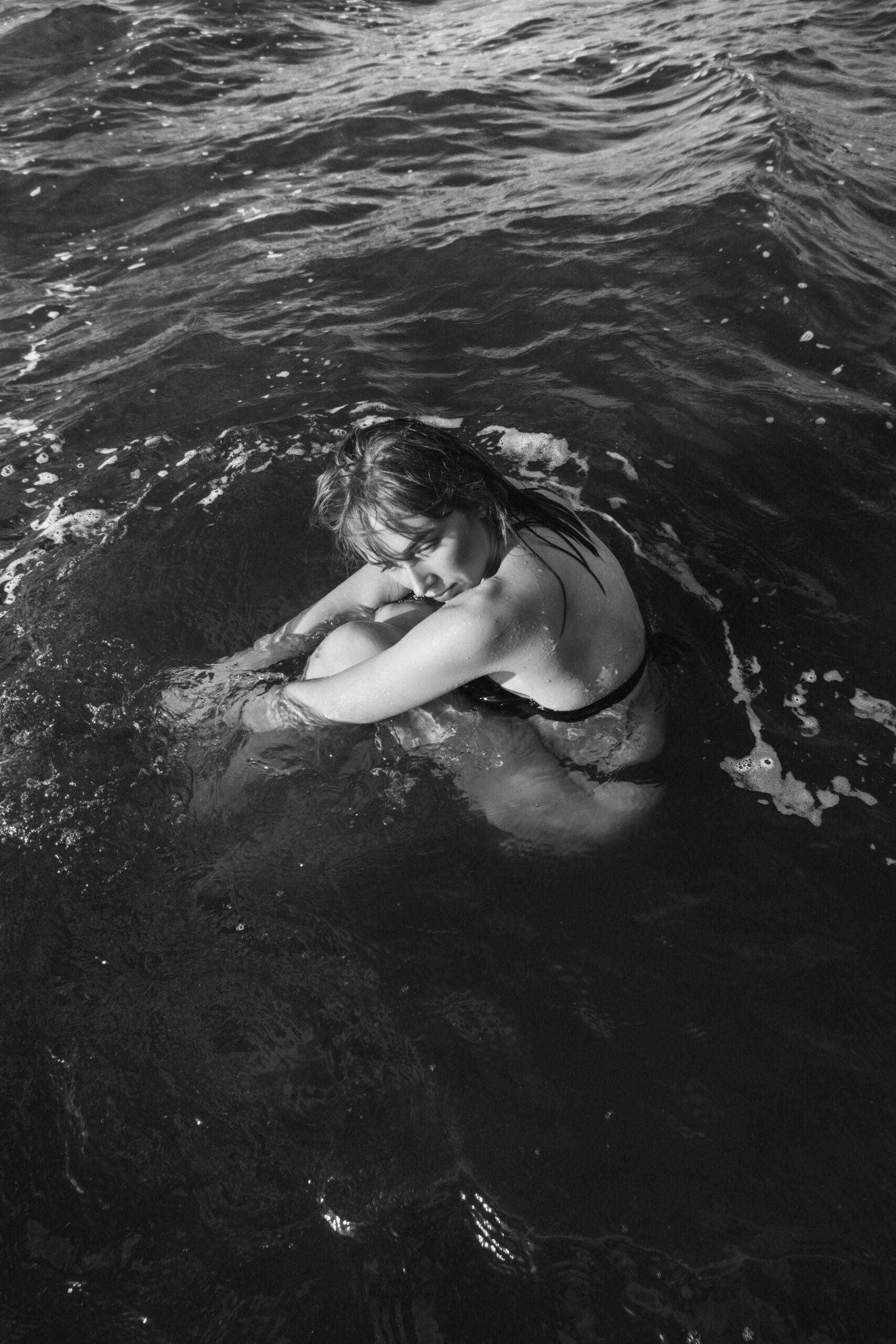 Black-and-white portrait of Yuliya seated in the sea, illustrating nature-led self-care storytelling.