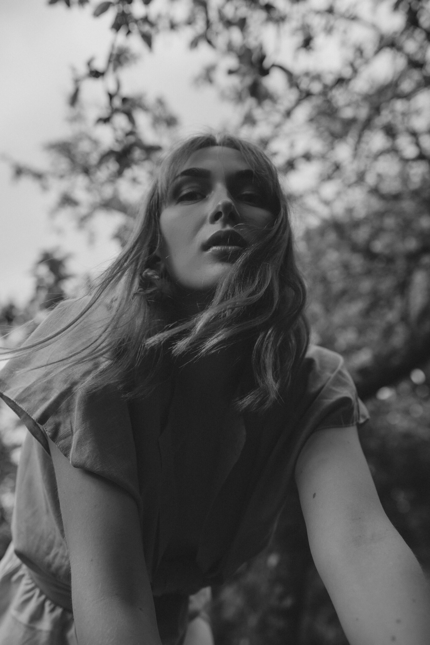 Low-angle black-and-white outdoor portrait framed by tree branches.