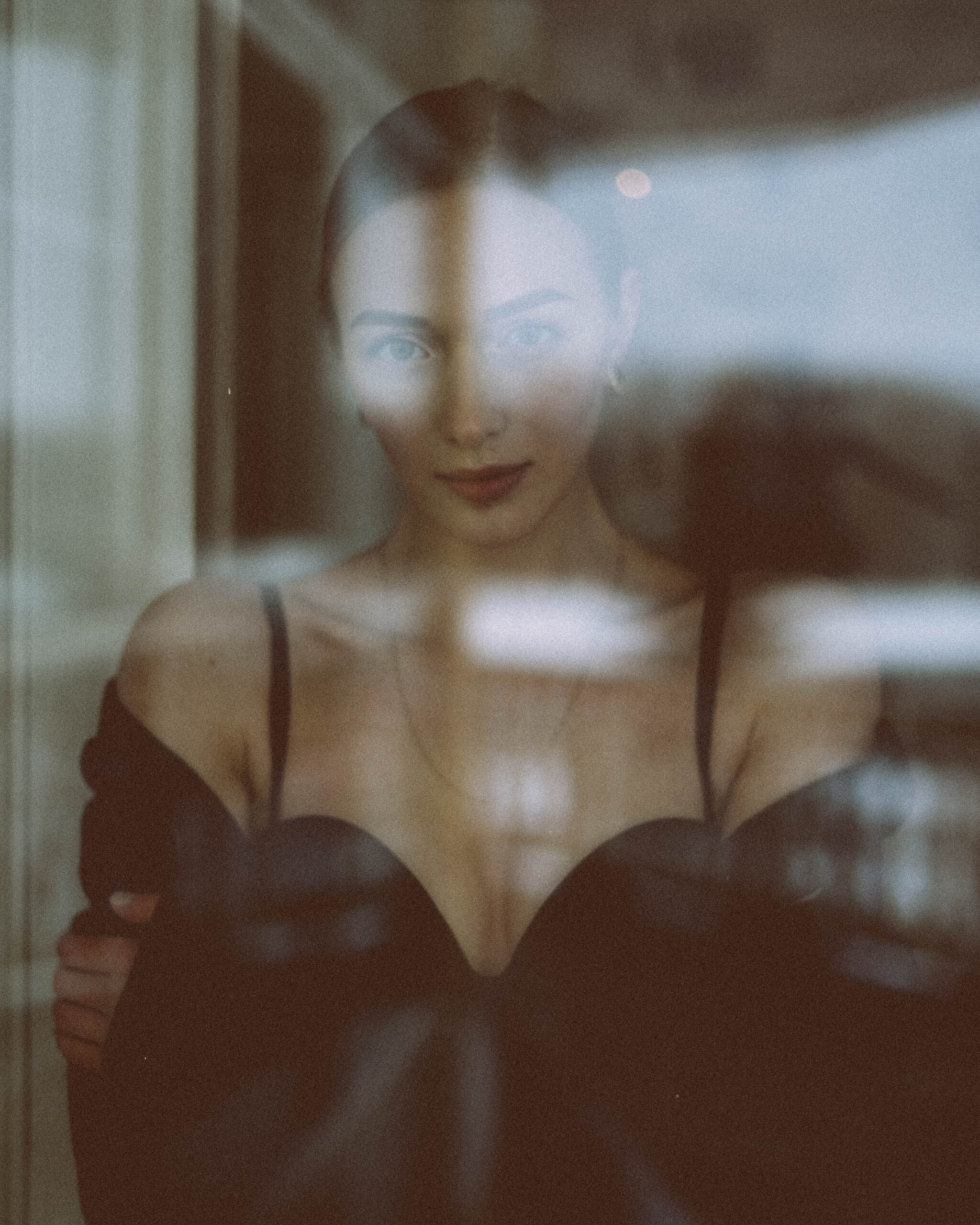 Editorial beauty portrait photographed through reflective glass in soft indoor light.